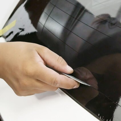 Corte preciso de lámina polarizada con bisturí NT Cutter sobre vidrio lateral de automóvil.